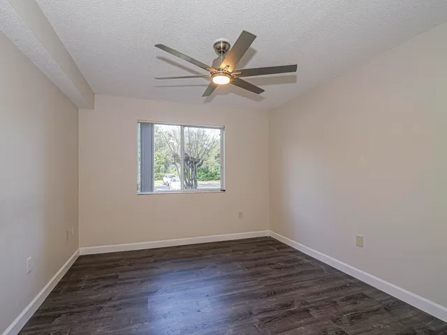 an empty room with wooden floor ceiling fan and window