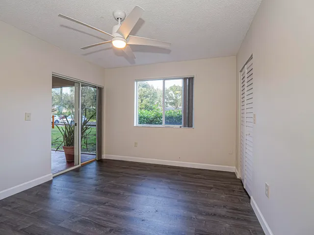 an empty room with wooden floor chandelier fan and windows