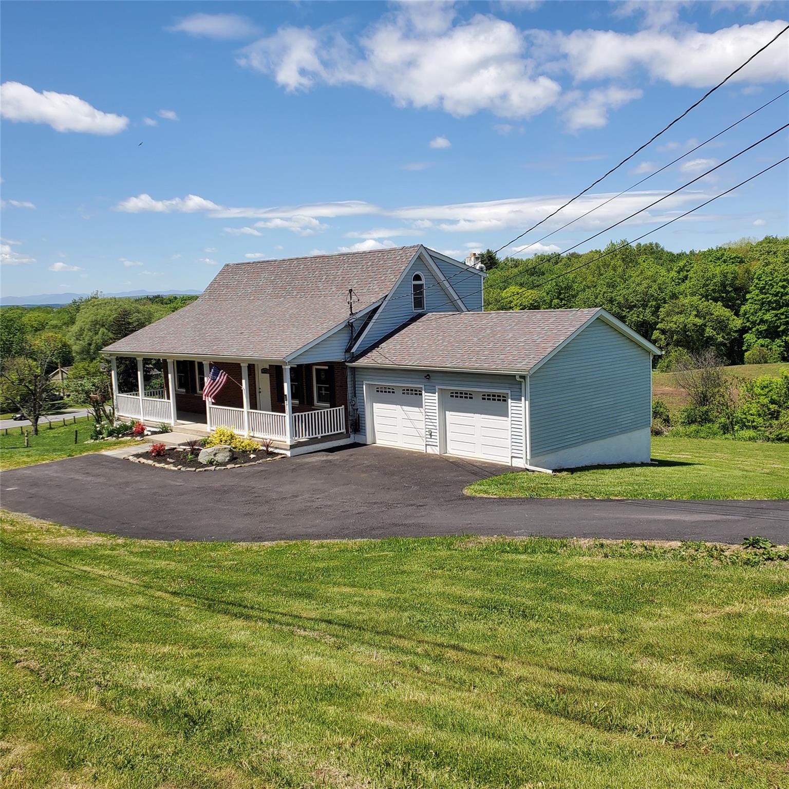 View of front of house featuring a porch, roof with shingles, an attached garage, a front lawn, and driveway
