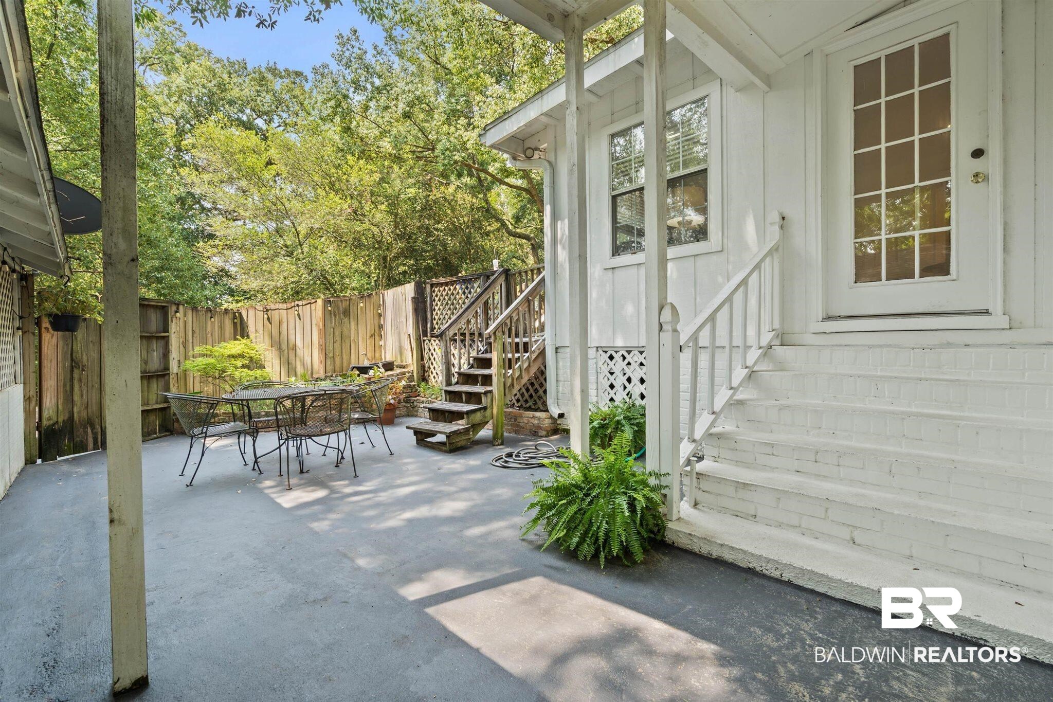 3751 Old Shell Road Mobile, AL 36608 - Photo 17 of 21 Spacious outdoor patio area featuring a privacy fence, mature trees, and direct access to an elevated exterior door with a multi-pane glass insert