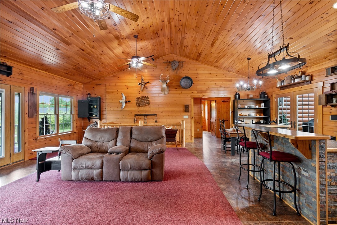 8205 Lake Road Seville, OH 44273 - Photo 8 of 35 Living room and part of kitchen with wood walls, carpet, vinyl floors, wooden ceiling, ceiling fan, and vaulted ceiling
