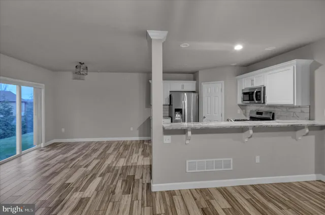 a living room with stainless steel appliances granite countertop a refrigerator oven a sink with wooden floors and cabinets