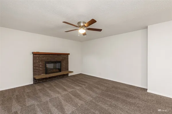 a view of an empty room with chandelier fan and fire place
