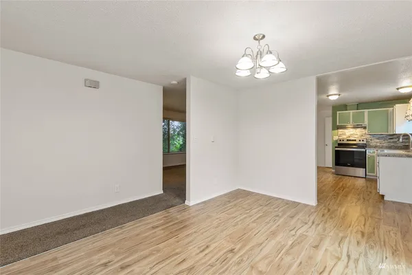 a view of an empty room with wooden floor and a kitchen