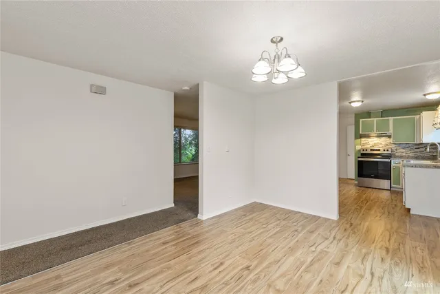 a view of an empty room with wooden floor and a kitchen