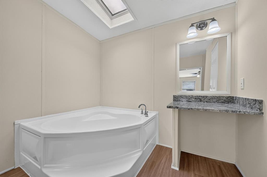 13405 Wheat Road Venus, TX 76084 - Photo 27 of 32 Corner soaking tub and a separate vanity featuring a stone countertop, framed mirror, and a two-light fixture