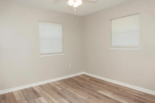 an empty room with a chandelier fan and wooden floor
