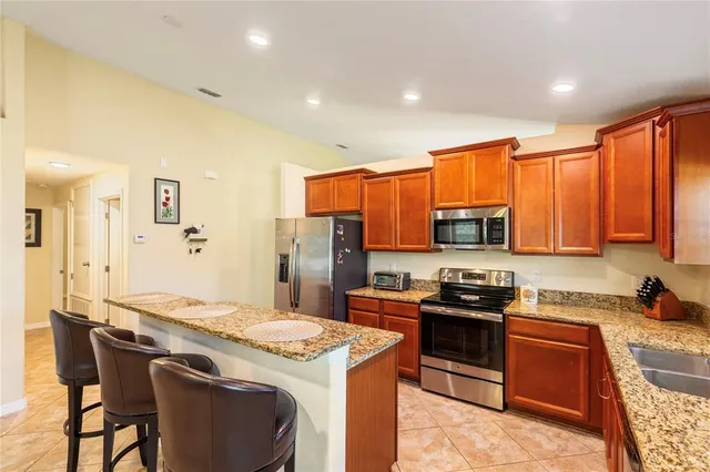 a kitchen with stainless steel appliances granite countertop a stove top oven a sink dishwasher and a refrigerator with wooden cabinets