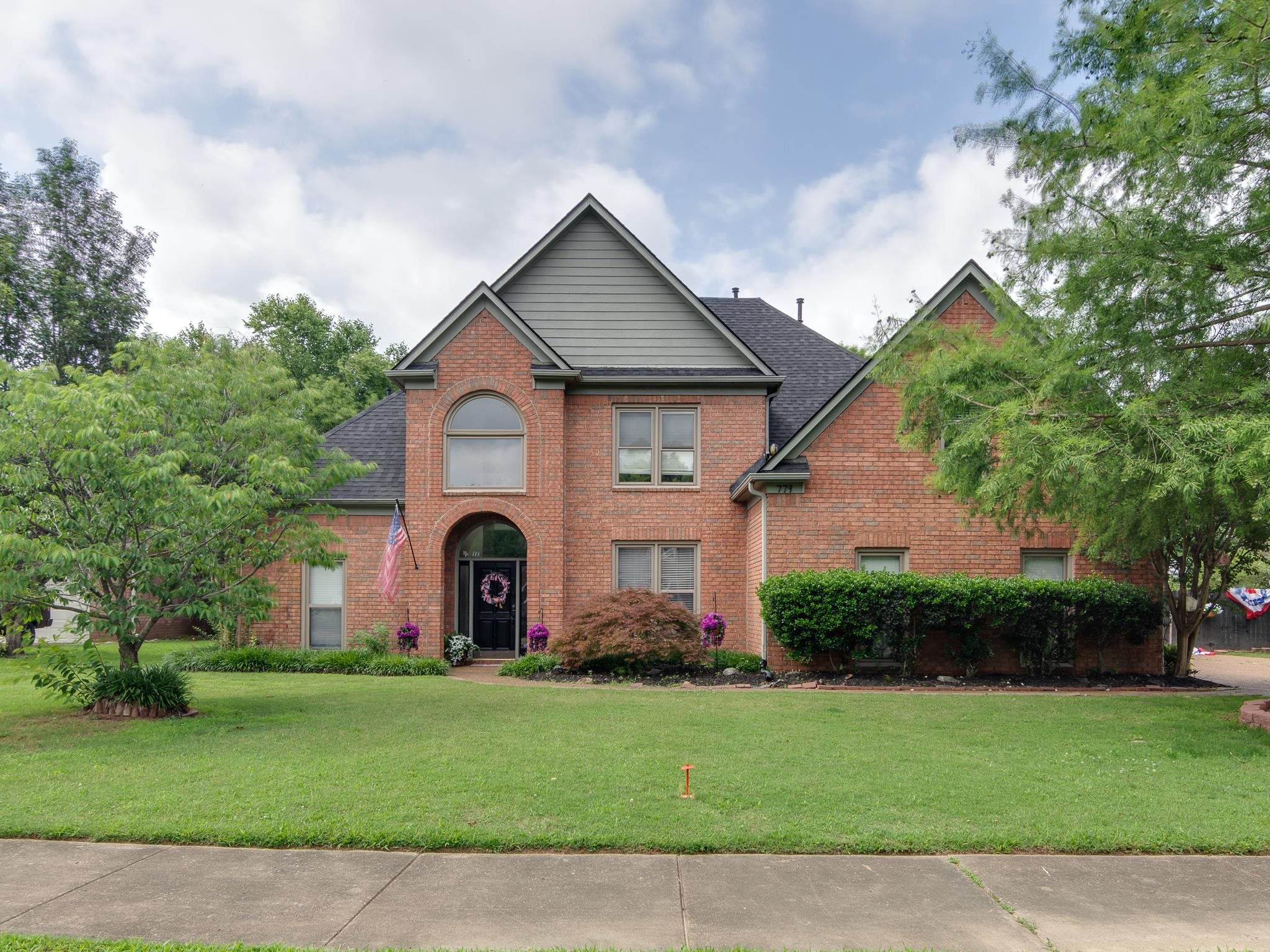 Traditional brick residence featuring a prominent arched entry, a dark shingle roof, and a gabled architectural detail with horizontal siding