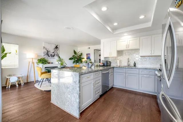 a kitchen with stainless steel appliances granite countertop a refrigerator a sink dishwasher a stove and white cabinets with wooden floor