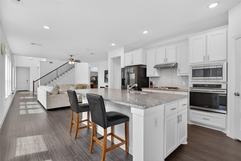 a kitchen with stainless steel appliances kitchen island granite countertop a stove top oven a sink dishwasher and a refrigerator with wooden floor