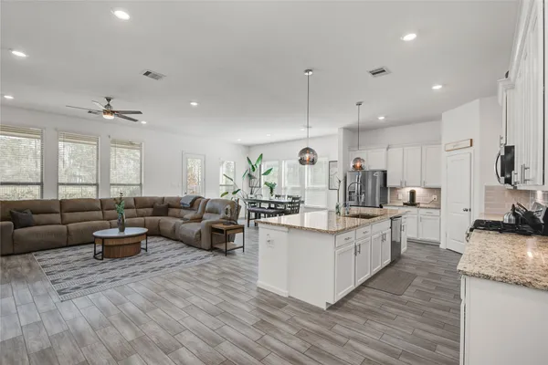 a large kitchen with stainless steel appliances lots of white cabinets a sink dishwasher a dining table and chairs with wooden floor