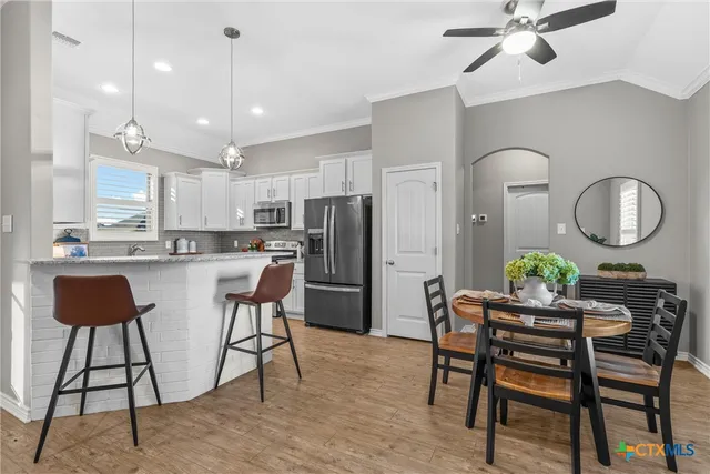 a kitchen with stainless steel appliances kitchen island granite countertop a dining table chairs and a refrigerator