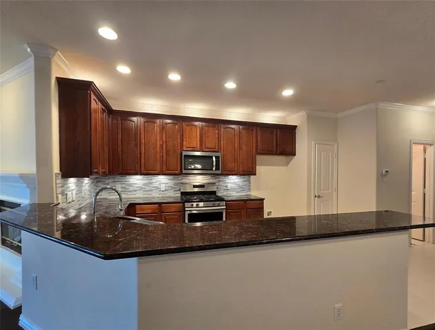 a large kitchen with stainless steel appliances a large counter top a stove and a refrigerator with wooden floor