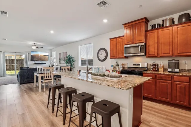 a open kitchen with stainless steel appliances granite countertop a stove top oven a sink dishwasher and white cabinets with wooden floor