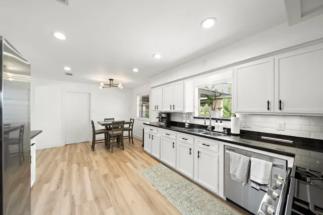 a kitchen with stainless steel appliances granite countertop a stove white cabinets a sink dishwasher and a stove with wooden floor