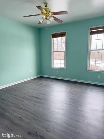 an empty room with wooden floor fan and windows