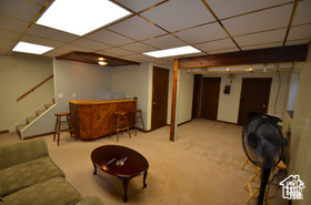 6874 South 595 East Midvale, UT 84047 - Photo 10 of 16 Living area featuring stairs, a bar, carpet, and a drop ceiling
