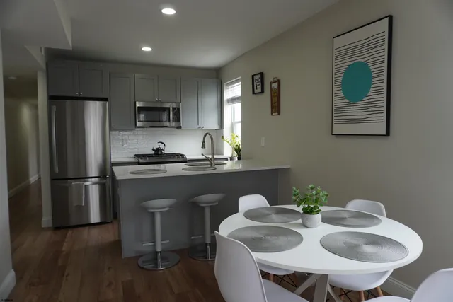 a kitchen with stainless steel appliances granite countertop a refrigerator a sink a stove a dining table and chairs with wooden floor