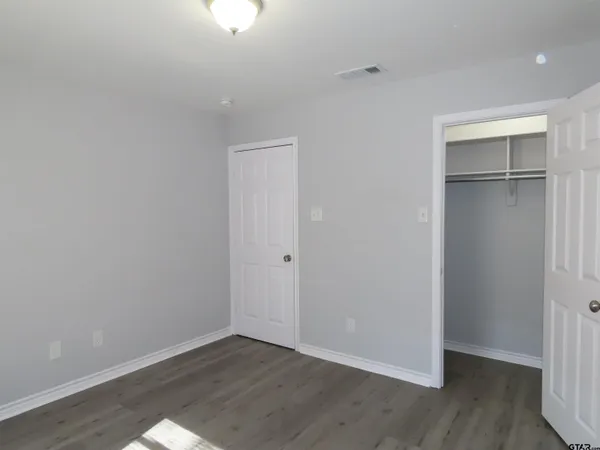 a view of an empty room with wooden floor closet and a window