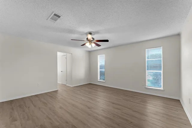 an empty room with wooden floor chandelier fan and windows