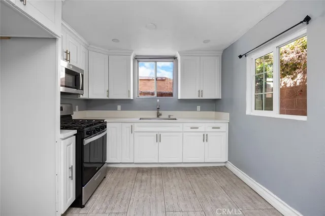 a kitchen with granite countertop white cabinets a window wooden floor and stainless steel appliances