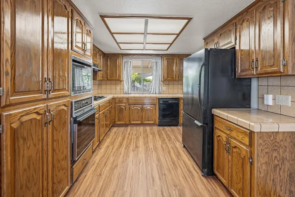 a kitchen with stainless steel appliances granite countertop a refrigerator a sink dishwasher a stove and white countertops with wooden floor
