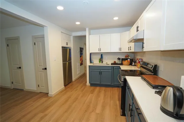 a kitchen with stainless steel appliances granite countertop a refrigerator a sink dishwasher a stove and white countertops with wooden floor