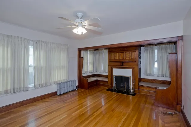 a view of an empty room with wooden floor fireplace and a window