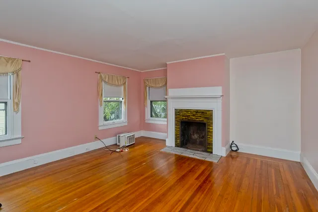a view of an empty room with wooden floor fireplace and a window