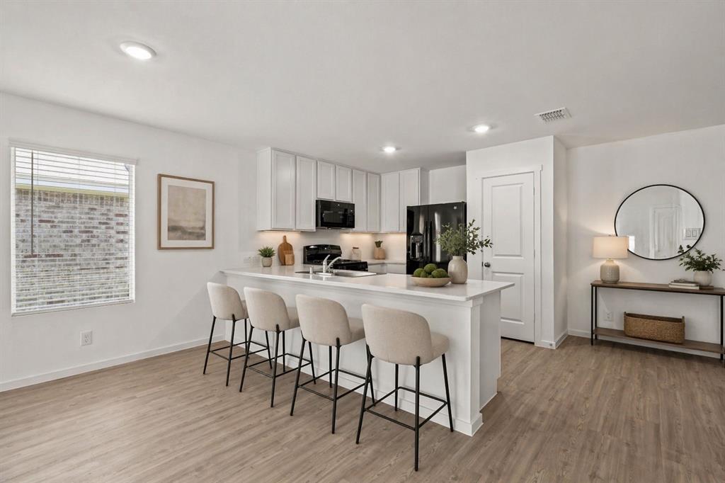 1138 Barbary Flds Street Forney, TX 75126 - Photo 8 of 25 Open-concept kitchen and living area featuring wood-finish flooring, white cabinetry, integrated black appliances, recessed lighting, and a kitchen island with seating