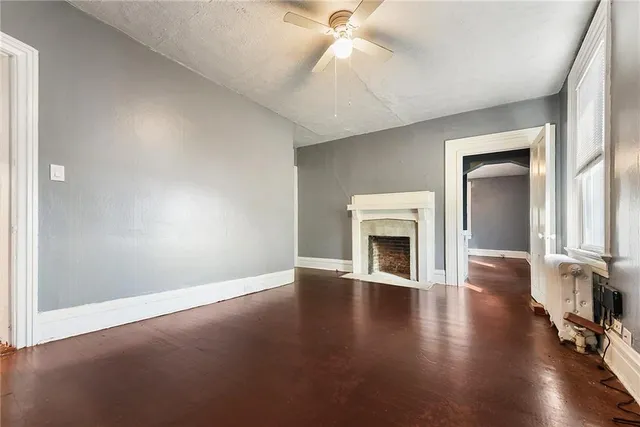 an empty room with fireplace wooden floor chandelier fan and windows