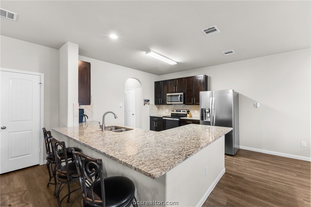 984 Crossing Drive Bryan, TX 77803 - Photo 9 of 29 a kitchen with granite countertop kitchen island stainless steel appliances a sink stove refrigerator and wooden floor