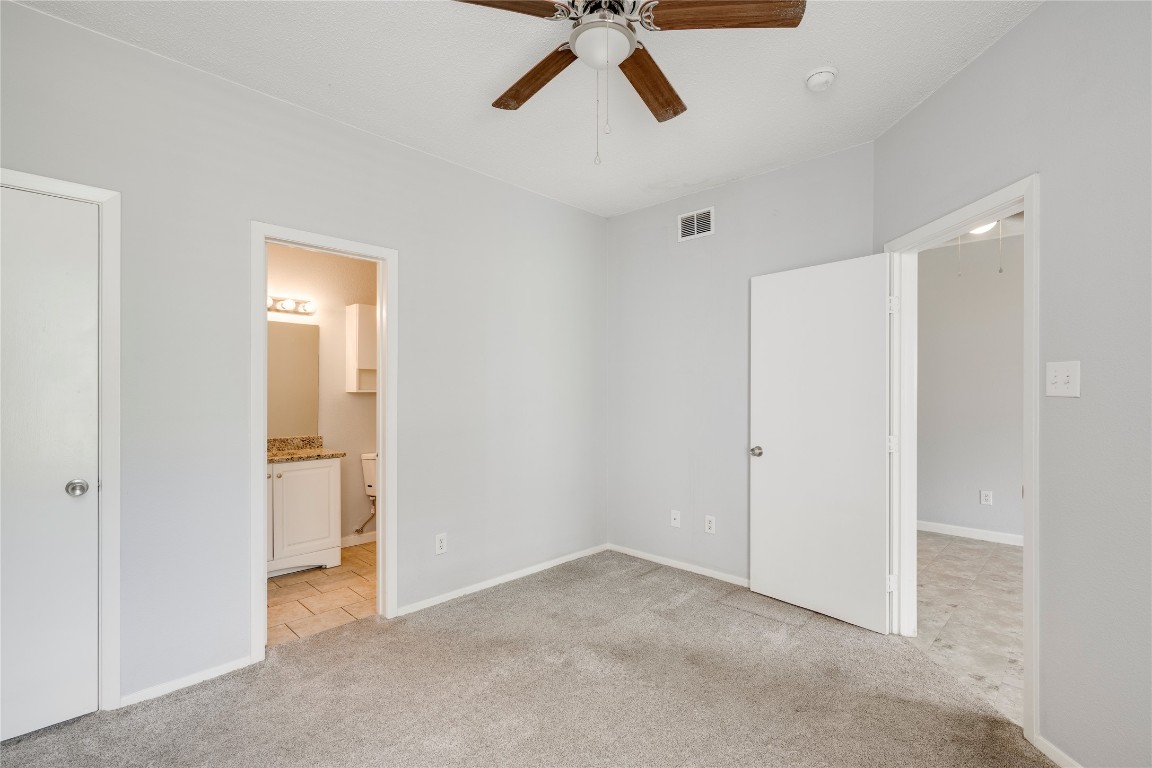 12166 Metric Boulevard, Unit 129 Austin, TX 78758 - Photo 14 of 38 Unfurnished bedroom featuring light carpet, ensuite bathroom, and a ceiling fan
