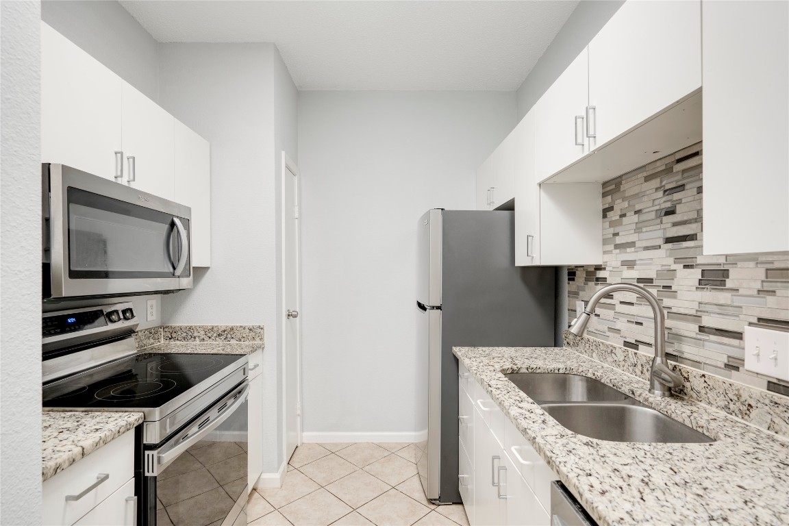 12166 Metric Boulevard, Unit 129 Austin, TX 78758 - Photo 22 of 38 Kitchen with stainless steel appliances, backsplash, white cabinets, and light stone countertops