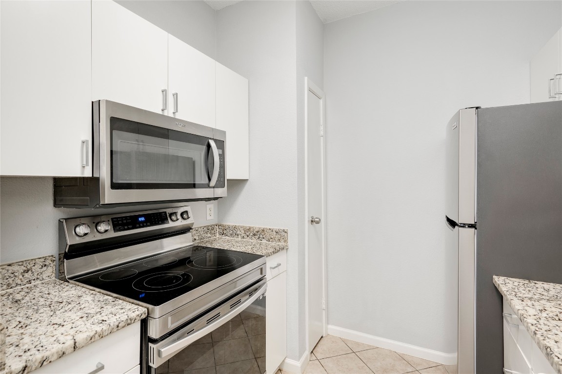 12166 Metric Boulevard, Unit 129 Austin, TX 78758 - Photo 23 of 38 Kitchen featuring appliances with stainless steel finishes, light tile patterned flooring, white cabinets, and light stone countertops