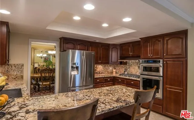 a kitchen with kitchen island granite countertop wooden cabinets a refrigerator a stove a sink and a oven