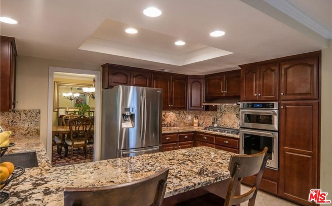 a kitchen with kitchen island granite countertop wooden cabinets a refrigerator a stove a sink and a oven