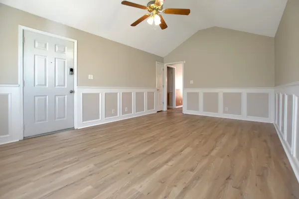 a view of an empty room with wooden floor and a ceiling fan