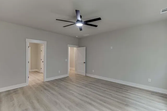 an empty room with wooden floor ceiling fan and windows