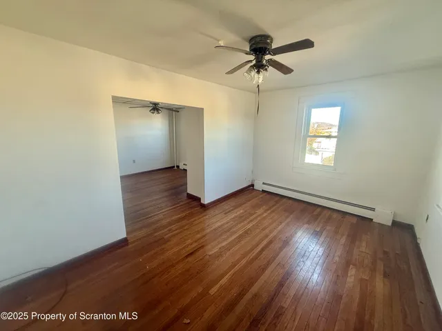 an empty room with wooden floor ceiling fan and windows