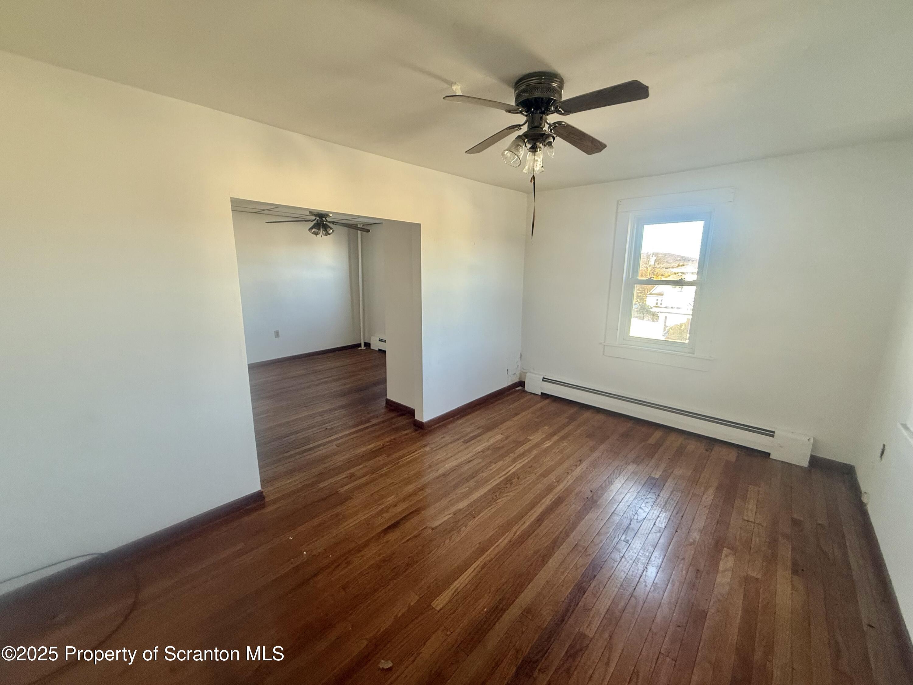 662 Simpson Street Throop, PA 18512 - Photo 2 of 9 an empty room with wooden floor ceiling fan and windows