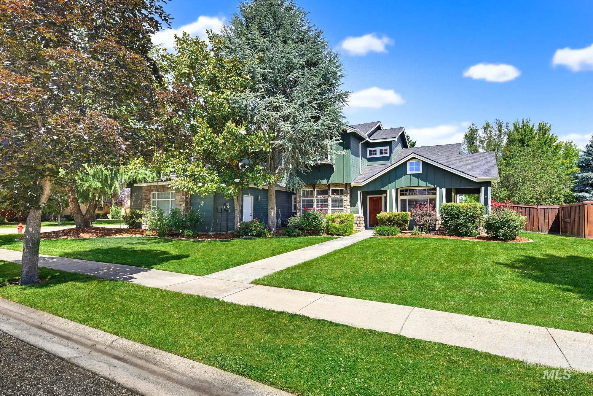 2172 West Cedar Grove Street Meridian, ID 83646 - Photo 1 of 49 Contemporary home exterior featuring a dark green facade with stone accents, a multi-gabled roofline, a vibrant red entry door, established landscaping, and a manicured lawn
