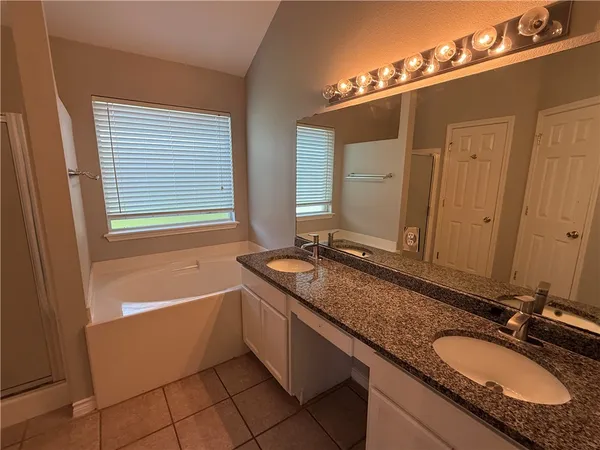 a bathroom with a granite countertop double vanity sink a mirror and a bathtub