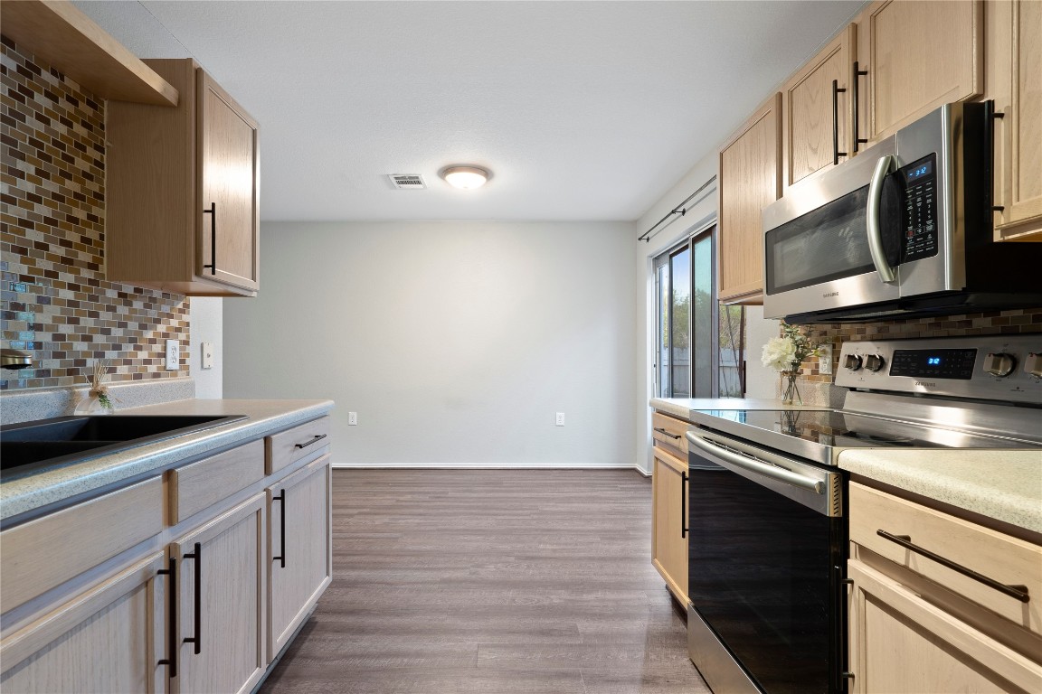 8609 Claude Court Austin, TX 78747 - Photo 3 of 30 a kitchen with stainless steel appliances a sink dishwasher a stove and a microwave oven with wooden floor