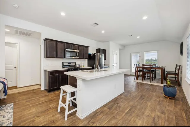 a kitchen with stainless steel appliances granite countertop a stove top oven a sink dishwasher a dining table and chairs with wooden floor