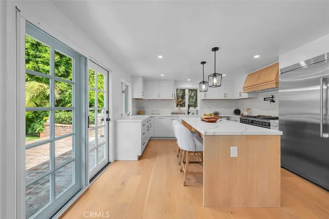 a kitchen with stainless steel appliances granite countertop a refrigerator a sink dishwasher a stove and a dining table with wooden floor