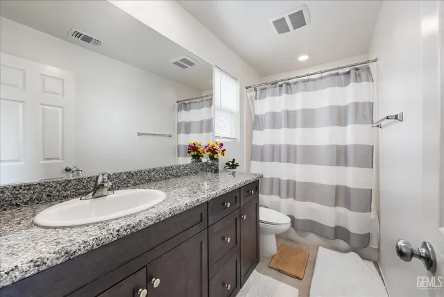 a bathroom with a granite countertop sink a toilet a mirror and shower curtain