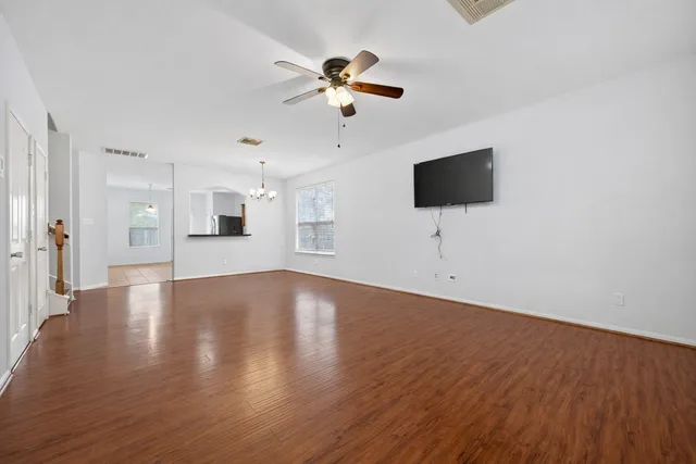 an empty room with wooden floor chandelier fan and windows