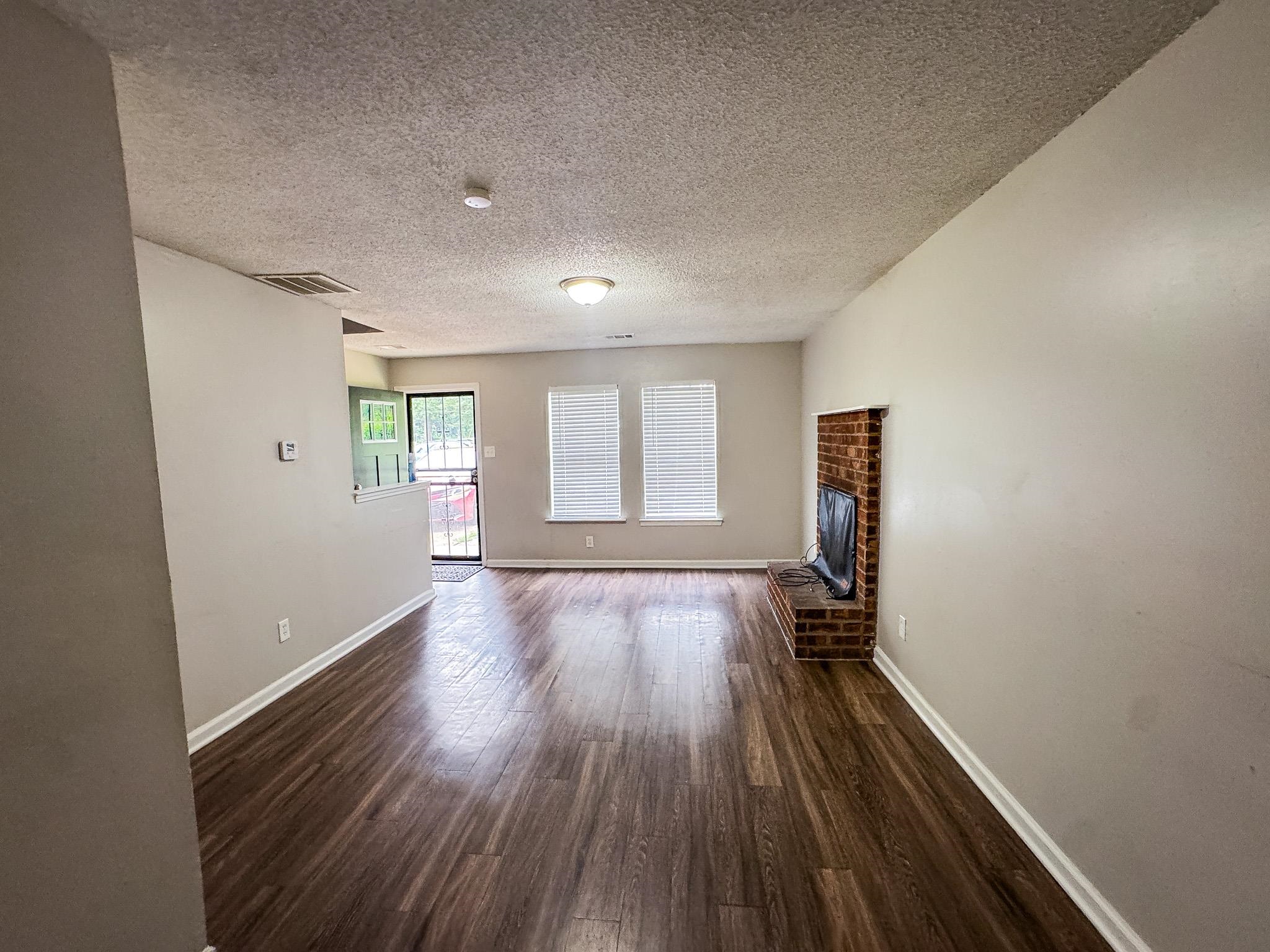 3592 Christine Road Memphis, TN 38118 - Photo 6 of 13 Spacious living area featuring wood-finish flooring, light neutral wall paint, and a brick-detailed hearth